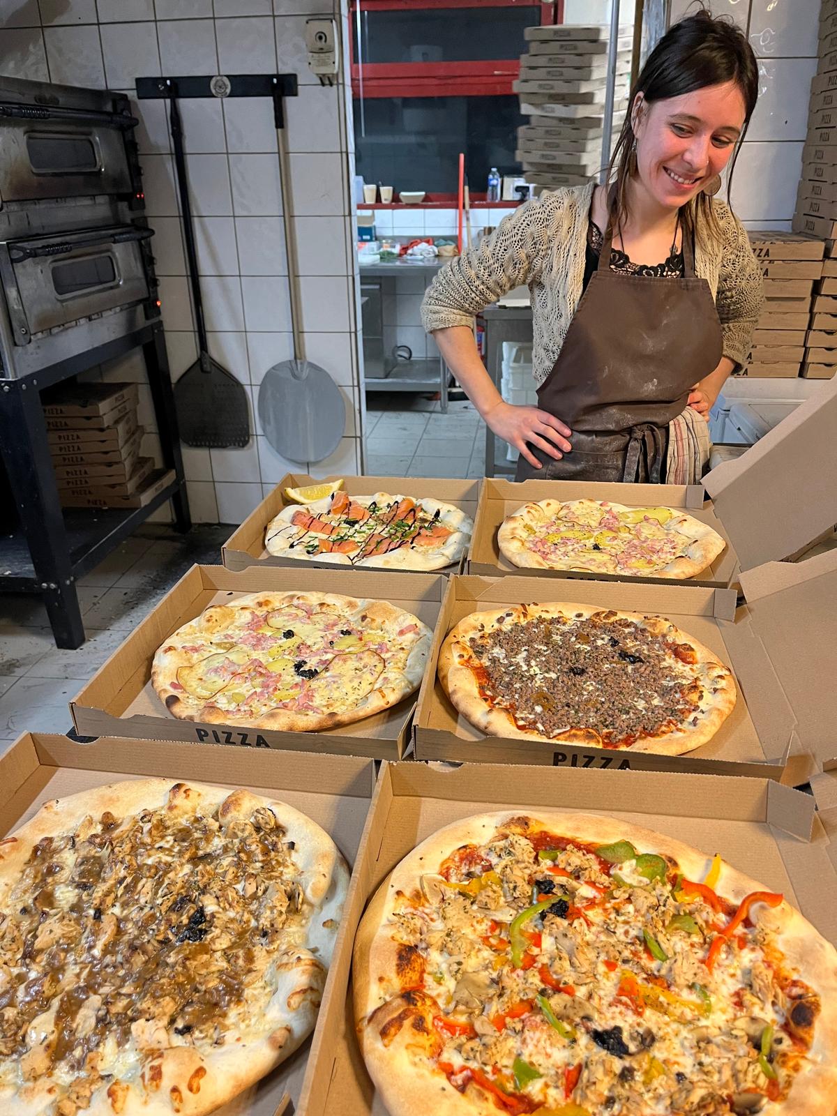 Une pizzaiola souriante devant six pizzas tout juste sorties du four